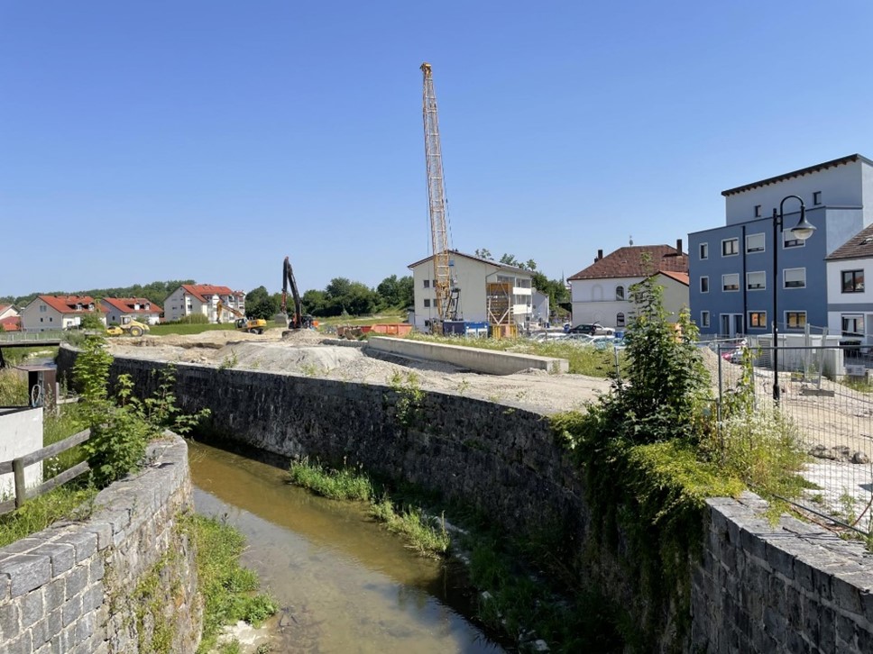 Abschnitt II - BA 04 – Bild 1 Baubeginn Bauabschnitt 4 (Blick Richtung Südost, von der Bachstraße Richtung Kreuzberger Weg Brücke). Im Vordergrund ist das bestehende Gerinne mit Hochwasserschutzmauern zu sehen, im Hintergrund beginnen die Aushubarbeiten für den neuen Abflussquerschnitt.